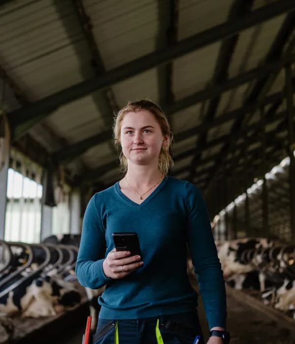 Woman in a cow stable smiling with technology at hand