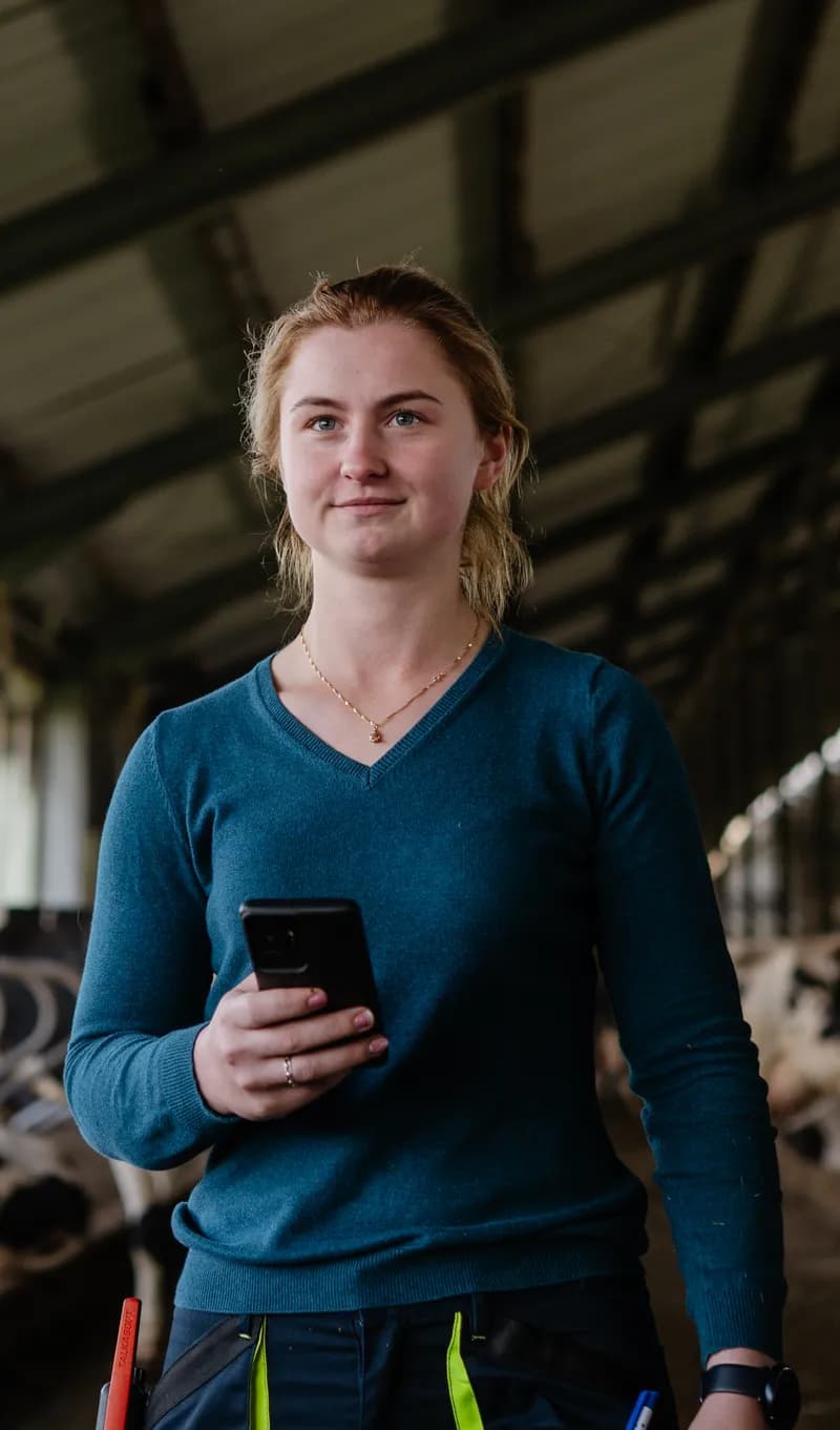 Woman in a cow stable smiling with technology at hand